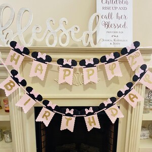May include: Pink and black Happy 2nd Birthday banner with Minnie Mouse ears and bows. The banner is strung up over a fireplace.