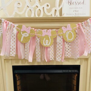 May include: A decorative banner with gold glitter Minnie Mouse heads spelling out a name, with pink bows and ribbons. The banner is strung with pink and gold polka dot fabric strips. Above the banner is a wooden sign that says "Blessed".