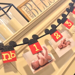 May include: A black and white Mickey Mouse themed baby milestone banner with red and yellow numbers and photos of a baby. The banner includes the letters "nb" for newborn, and the numbers 1, 2, and 3.