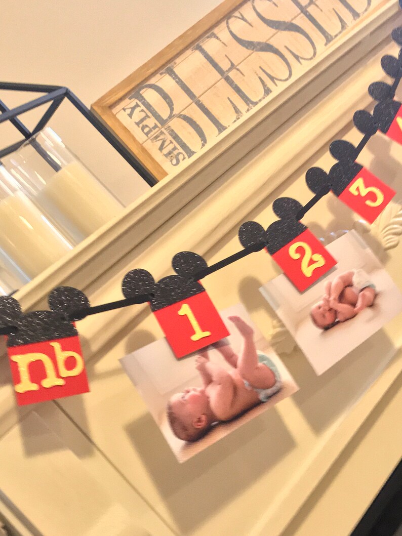 May include: A black and white Mickey Mouse themed baby milestone banner with red and yellow numbers and photos of a baby. The banner includes the letters "nb" for newborn, and the numbers 1, 2, and 3.