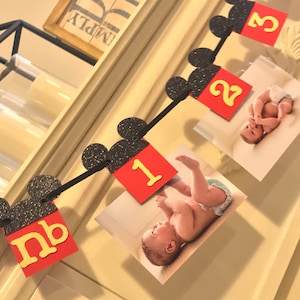 May include: A black and red Mickey Mouse themed banner with a photo of a baby at each month. The banner includes the numbers 1, 2, 3, 4, and nb.
