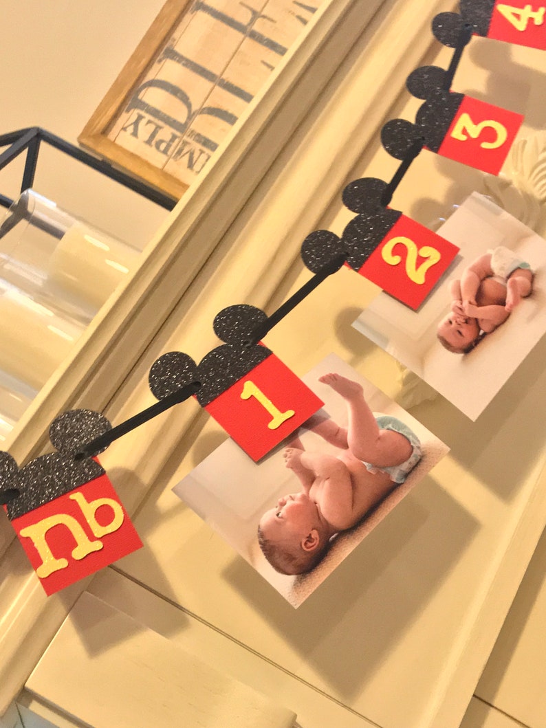 May include: A black and red Mickey Mouse themed banner with a photo of a baby at each month. The banner includes the numbers 1, 2, 3, 4, and nb.