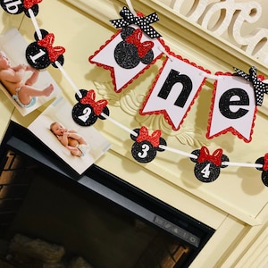 May include: A black and red Minnie Mouse themed banner with the word "one" in white letters. The banner has red and white polka dots and black glitter. There are also black and red Minnie Mouse heads with numbers 1 through 4 on them.
