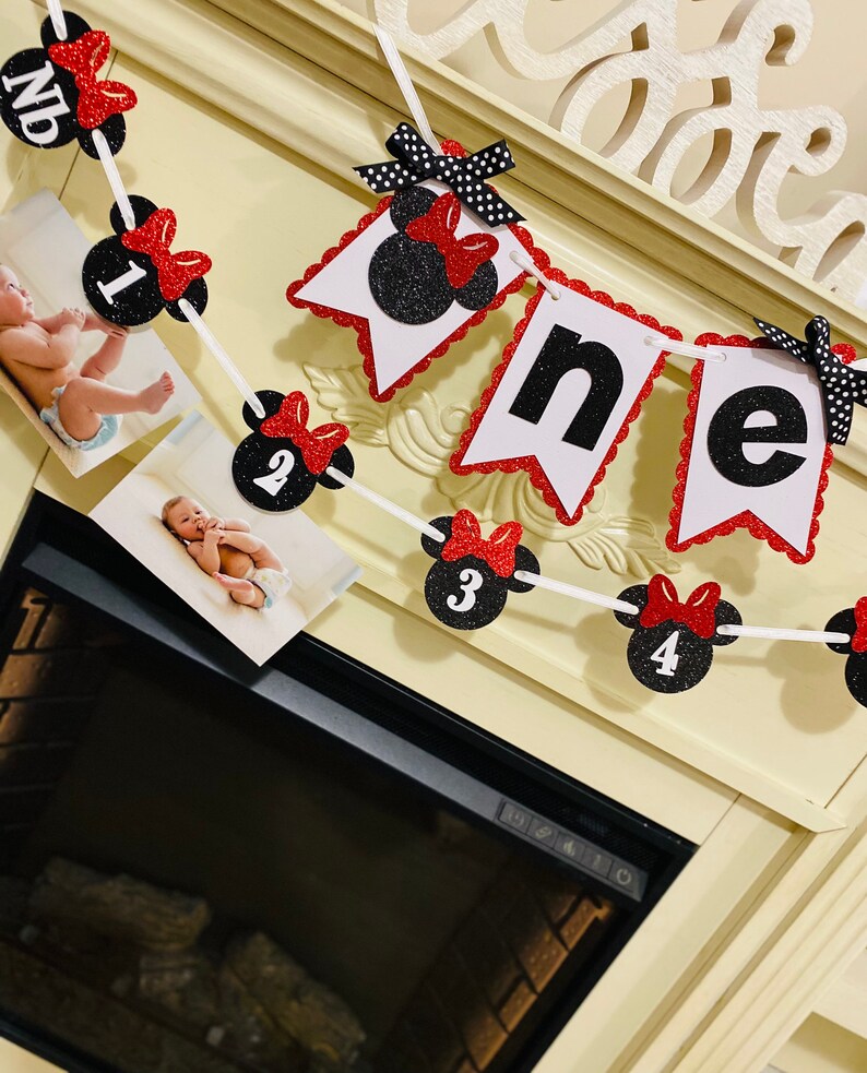 May include: A black and red Minnie Mouse themed banner with the word "one" in white letters. The banner has red and white polka dots and black glitter. There are also black and red Minnie Mouse heads with numbers 1 through 4 on them.