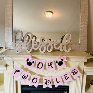 May include: Pink and white banner with the words "Oh Boy" and "Twinkle" with a Mickey Mouse head on each end. The banner is hanging above a fireplace.