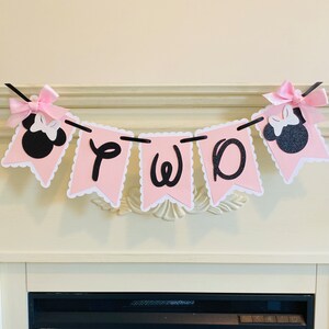 May include: Pink and black banner with the word "TWO" in black letters and two black and pink Minnie Mouse heads on either end.
