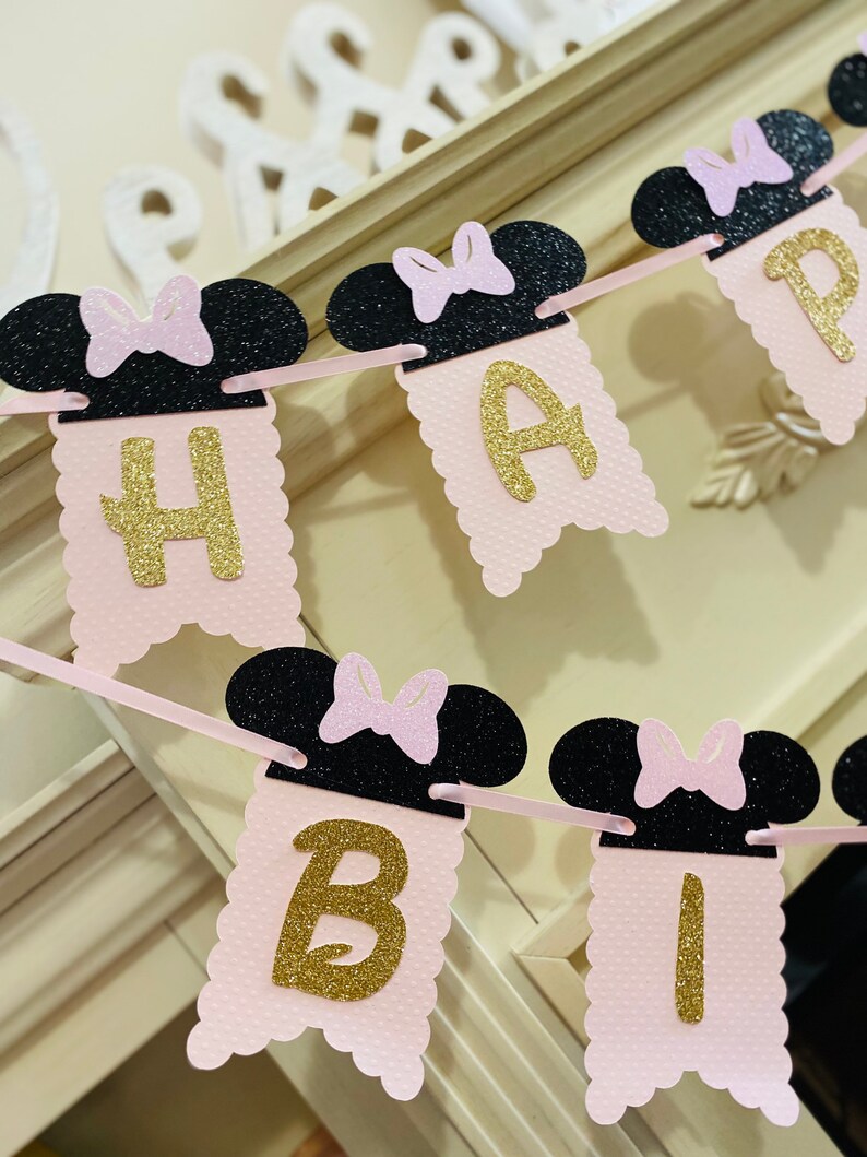 May include: Pink and black banner with gold glitter letters spelling "Happy Birthday". The banner features black mouse ears with pink bows.
