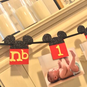 May include: A black and red Mickey Mouse themed banner with black glitter ears and red squares with yellow letters. The banner says "nb 1".
