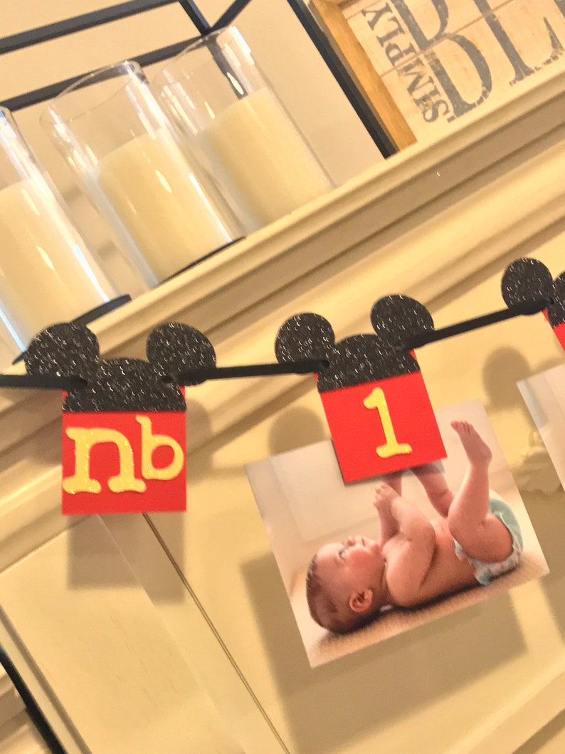 May include: A black and red Mickey Mouse themed banner with black glitter ears and red squares with yellow letters. The banner says "nb 1".