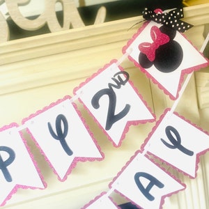 May include: Pink and white banner with black letters that say "Happy 2nd Birthday". The banner has a pink scalloped edge and a black and white polka dot bow with a pink bow on top.
