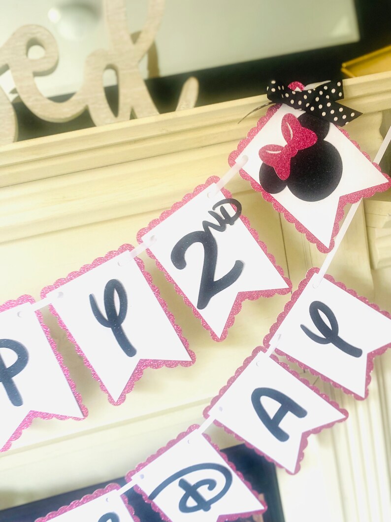 May include: Pink and white banner with black letters that say "Happy 2nd Birthday". The banner has a pink scalloped edge and a black and white polka dot bow with a pink bow on top.