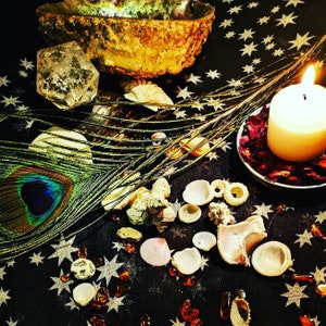 May include: A white candle with a flame sits on a black background with a peacock feather, seashells, and crystals.