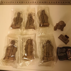 May include: Six unopened plastic bags containing small brown Star Wars character figurines. The bags are labelled with the company name and address.  A brown R2-D2 figurine is visible on the right side of the image.  The text on the bag reads: "General Mills Ltd, 22 Station Road, Gerrards Cross, Buckinghamshire, SL9 8EL.  Please retain address for future reference."