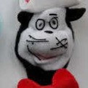 Op de afbeelding: Een pluche speelgoed van de Kat in de Hoed uit de film "De Kat in de Hoed". Het speelgoed draagt een rood-wit gestreepte hoed met de tekst "The Cat in the Hat Movie" erop. Het speelgoed heeft een rode strik en een zwart-wit gezicht.