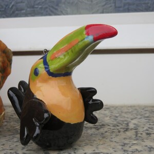 Könnte beinhalten: Eine Keramik-Toukan-Figur mit schwarzem Körper, grün-gelb-rot-blauem Schnabel und schwarzen Flügeln.