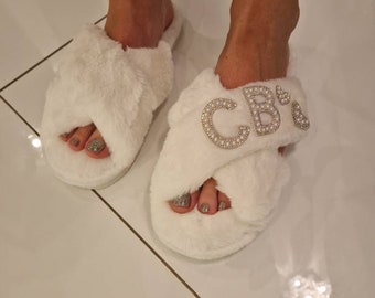 May include: White faux fur slippers with a criss-cross strap and the initials "CB" in rhinestones.
