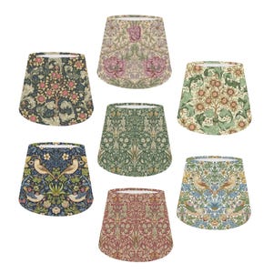 May include: Seven different lampshades featuring floral patterns. The lampshades are all the same shape and size, but they have different colours and designs. The designs include birds, flowers, and leaves.