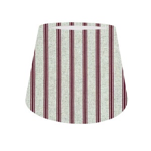 May include: A white lampshade with vertical burgundy stripes. The lampshade is made of a textured fabric.