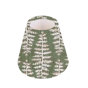 May include: A green fabric bib featuring a white fern pattern. The bib has an oval opening at the top and a rounded base. The fern design is repeated vertically across the fabric.