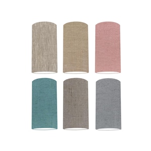 May include: Six cylindrical lampshades in a range of colours: light grey, beige, pink, teal, taupe, and grey. Each lampshade has a textured fabric appearance and a rounded top and bottom. The lampshades are arranged in two rows of three.