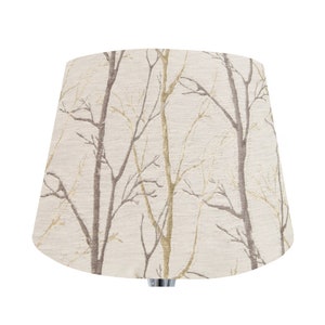 May include: A beige lampshade with a pattern of brown and gold branches.