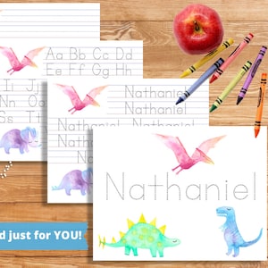 Può includere: Materiale didattico a tema dinosauri ad acquerello. Include fogli di esercizi di scrittura con dinosauri e pterodattili, pagine per tracciare l'alfabeto e fogli per tracciare i nomi. Sono visibili anche una mela rossa e pastelli.