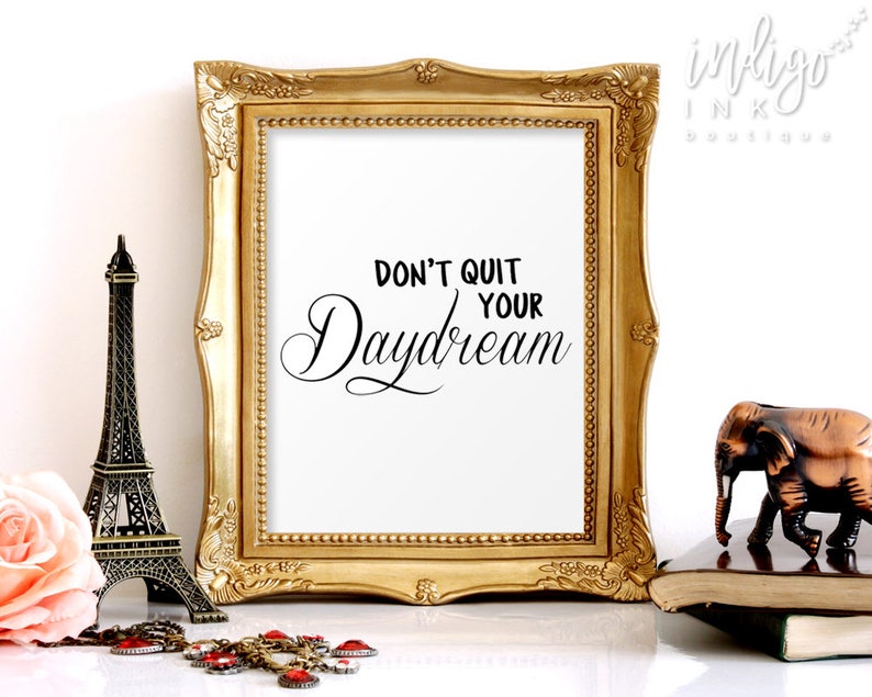 May include: A gold framed print with the text "Don't quit your daydream" in black calligraphy on a white background.