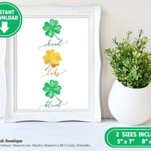 K&ouml;nnte beinhalten: Druckbare Wandkunst mit drei gr&uuml;nen Kleebl&auml;ttern mit goldenen Akzenten. Die Kleebl&auml;tter sind vertikal angeordnet, mit den W&ouml;rtern "charmed", "lucky" und "blessed", die in Kursivschrift unter jedem Kleeblatt stehen.