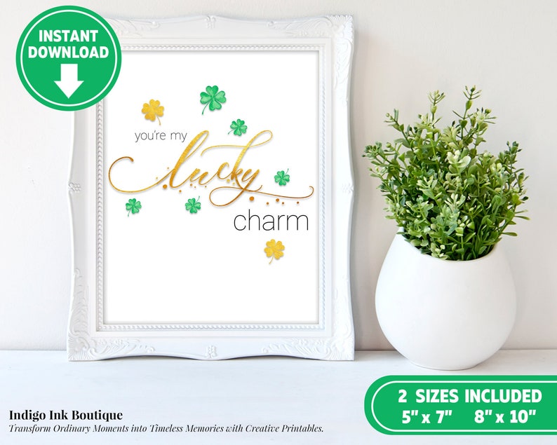 May include: Printable art print with gold lettering that says "you're my lucky charm" with green shamrocks scattered around the text. The print is framed in a white frame.