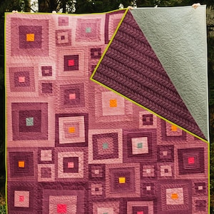 Peut inclure: Une courtepointe avec un motif de patchwork composé de carrés de différentes tailles et nuances de violet, rose et orange. La courtepointe est matelassée avec un motif de petits carrés et est bordée d'une bordure verte.
