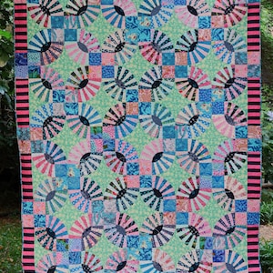May include: A patchwork quilt with a variety of colourful fabrics. The quilt is made up of squares and circles, and the colours include pink, blue, green, and black. The quilt is bordered with a black and pink striped fabric.