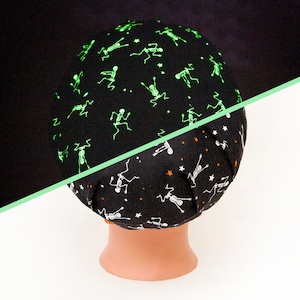 May include: A black Halloween skull cap with a repeating pattern of glowing green skeletons. The bottom half of the cap features a similar design with white skeletons and orange stars. The cap is displayed on a mannequin head.
