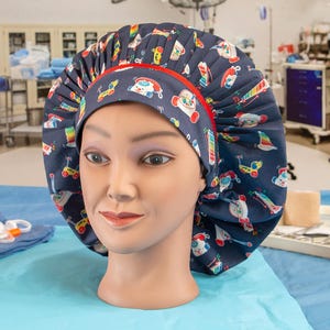 May include: A blue surgical cap with a red trim and a colorful toy pattern. The cap is made of a soft, comfortable fabric and is designed to be worn in a hospital or medical setting.