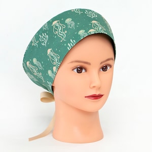 May include: A green surgical scrub hat with a white jellyfish pattern. The hat has a tie at the back.