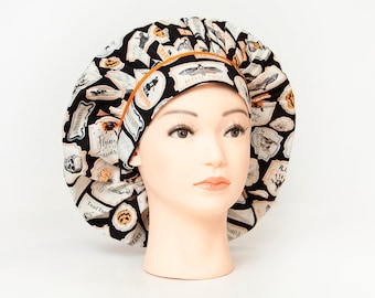 May include: A black and white Halloween-themed bouffant scrub hat with an orange trim. The hat features various labels with spooky illustrations and text, including "Flying Lessons" and "Toad Tears". The hat is displayed on a mannequin head.