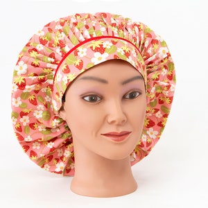 May include: A pink and red patterned shower cap with a red trim. The cap is made of fabric and has a gathered design.