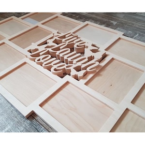 Può includere: Una cornice per foto in legno con 12 cornici individuali, ciascuna con un bordo bianco. La cornice è progettata per contenere foto e ha le parole "Live Laugh Love" ritagliate al centro.