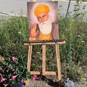 May include: A painting on an easel of a man with a yellow turban and beard, wearing a yellow robe. The painting is set against a light brown background.