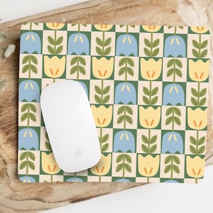 May include: A white computer mouse rests on a floral patterned mousepad. The mousepad features a repeating pattern of blue and yellow tulip-like flowers with green stems and leaves against a cream and green checkered background. The mouse is a standard size.