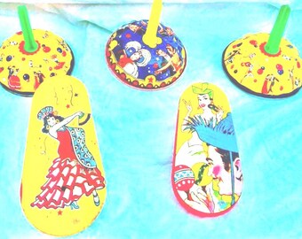 May include: A collection of vintage spinning tops and decorative cutouts. The tops have yellow and blue designs with green and yellow handles. The cutouts feature illustrations of dancers in red dresses and other figures.