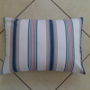 Könnte beinhalten: Ein weißes Kissen mit blauen und roten Streifen. Das Kissen ist aus einem weichen, gewebten Stoff.