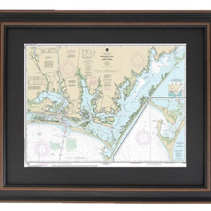May include: A framed nautical chart of the Beaufort Inlet and Core Sound area. The chart is printed in black and white with blue and green accents. The chart is framed in a dark brown wood frame with a black mat.