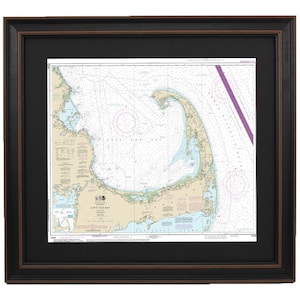 May include: A framed nautical chart of Cape Cod Bay, Massachusetts. The chart is printed in black and white with blue and green accents. The chart includes details of the coastline, waterways, and navigational aids. The chart is framed in a black frame with a brown mat.