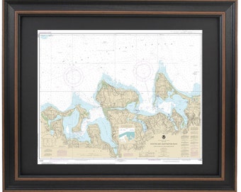 May include: A framed nautical chart of Oyster and Huntington Bays, New York. The chart is printed in black and white and shows the coastline, islands, and waterways of the area. The chart is titled "Oyster and Huntington Bays" and includes the text "United States Coast Guard Notice to Mariners No. 1/2019".