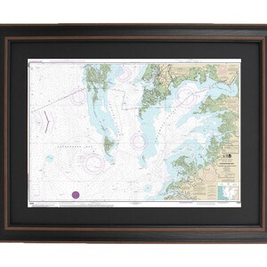 May include: A framed nautical chart of Chesapeake Bay, Virginia, with detailed markings and a compass rose. The chart is printed on white paper and framed in a black frame with a brown inner border.