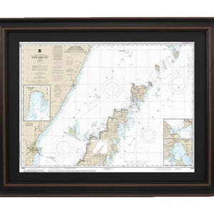 May include: A framed nautical chart of Little Sturgeon Bay, Wisconsin, with a black frame and a brown mat. The chart shows the shoreline, waterways, and depths of the bay.
