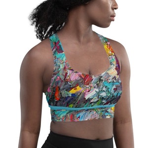 May include: A colorful sports bra with a bright abstract paint splatter design. The bra has a blue band across the bottom and a racerback style.