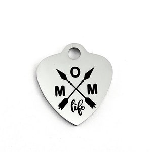 May include: Silver heart-shaped charm with a black inscription that reads "MOM life" with two crossed arrows and the letter "O" in the center.