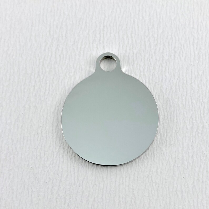 May include: A silver round blank tag with a hole at the top for attaching a chain or string.