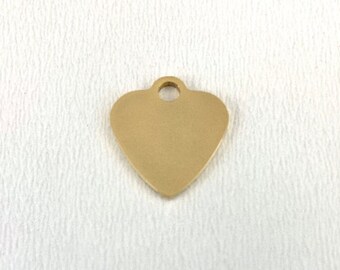 Könnte beinhalten: Ein goldfarbenes, herzförmiges Metallschild mit einem Loch oben zum Anbringen einer Kette oder eines Rings.